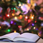 Open book in front of a decorated christmas tree. Photo by Andreea Radu on Unsplash. 
