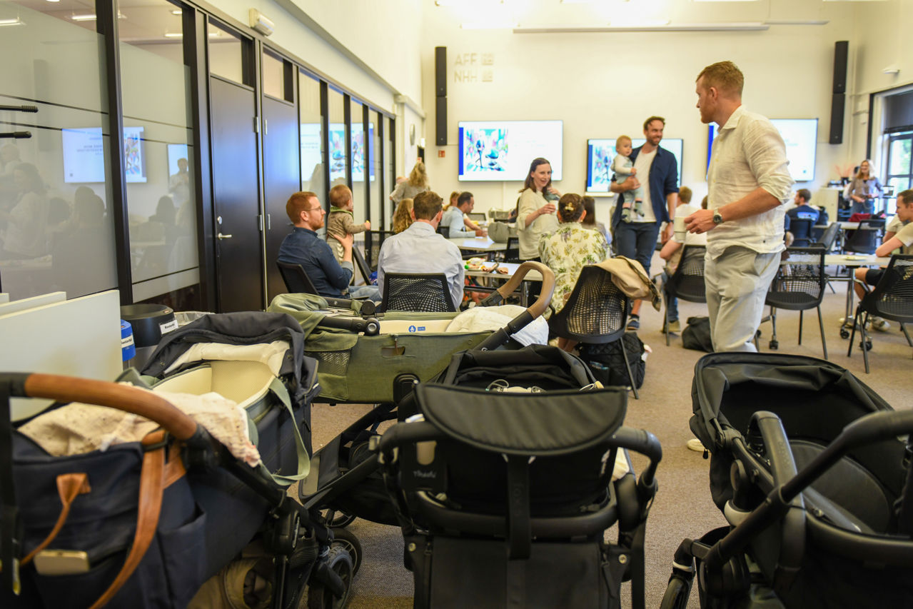 3 barnevogner i forgrunnen, og en rekke foreldre med barn rundt bord i et klasserom på NHH i Oslo.