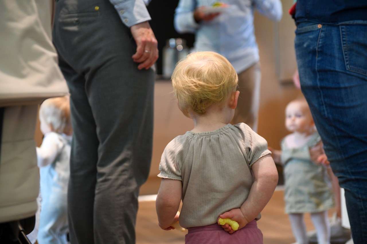 Bilde av en baby bakfra som holder en maizpuff (baby snacks) bak ryggen.