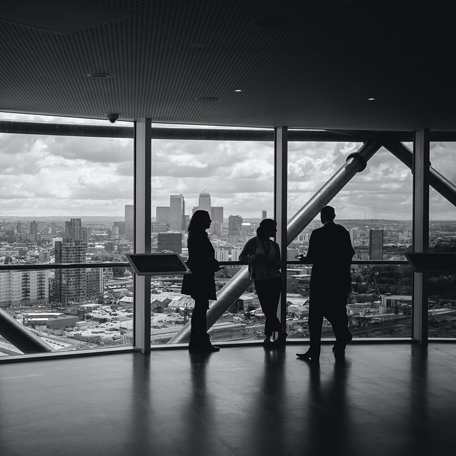 Three people watching the city skyline from a large window. Photo: Unsplash