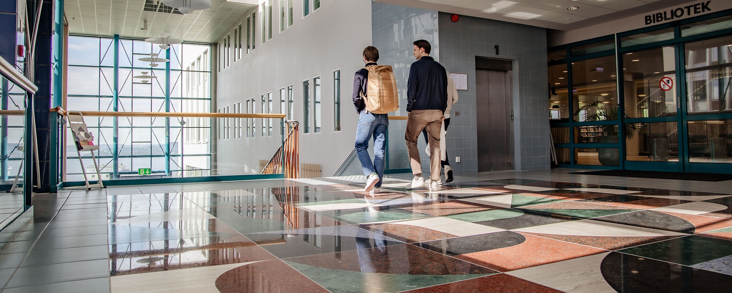 Two students wearing backpacks are walking passed the library towards a staircase at NHH's campus.