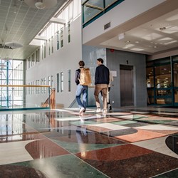 To elever med sekk på ryggen går forbi NHH sitt bibliotek på vei mot trappene ned til første etasje. 