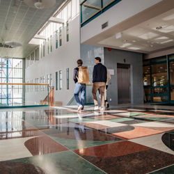 Two students wearing backpacks are walking passed  the library towards a staircase at NHH's campus.