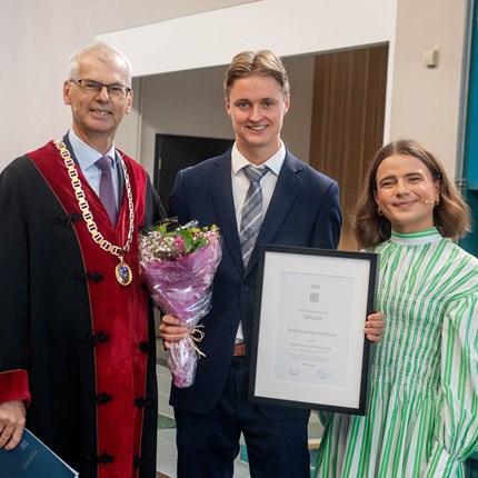 Prize winner with diploma and flower, next to him stands rector and the student representative.