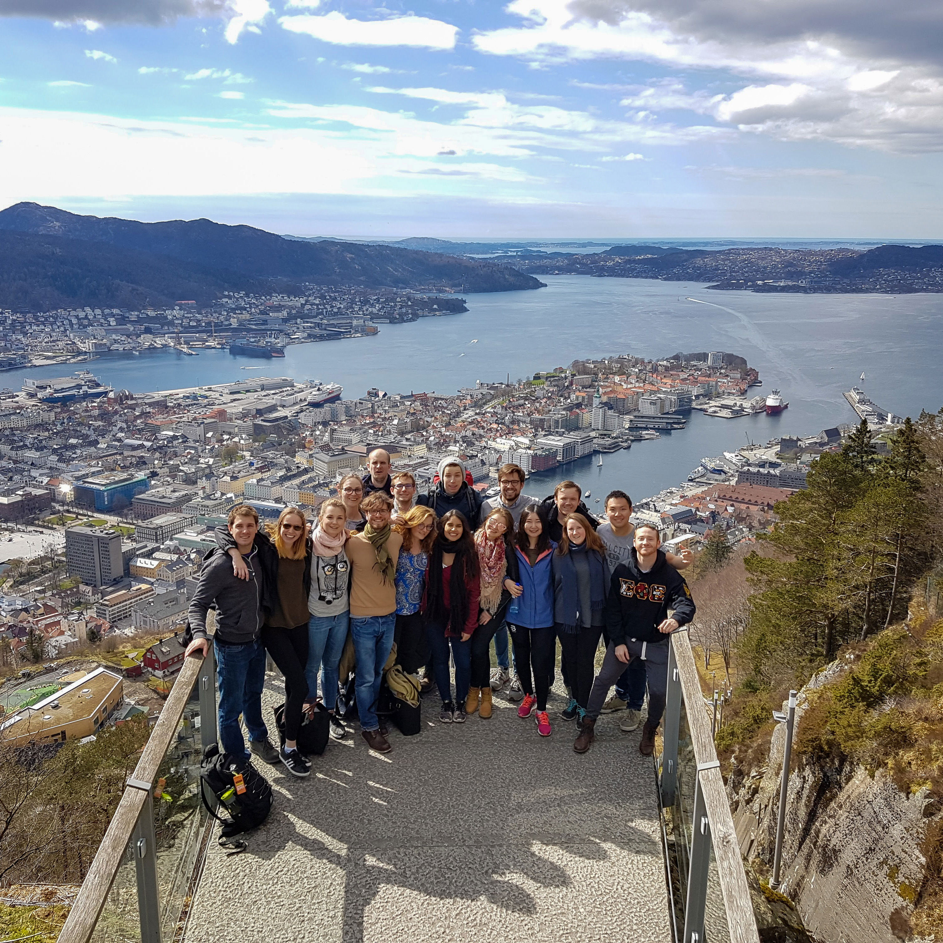 A group of students gathered for a group photo at the top of Mt Fløyen with the city of Bergen in the background.