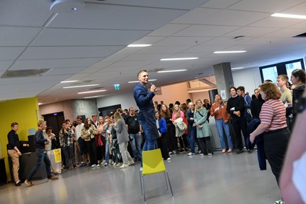 Steffen standing on a chair talking to a big group of students