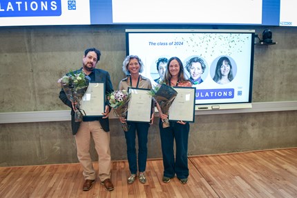 Carsten, Therese and Kristin in a row on stage, holding diplomas and flowers