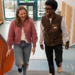 Two smiling students walking up a staircase at the Norwegian School of Economics (NHH).