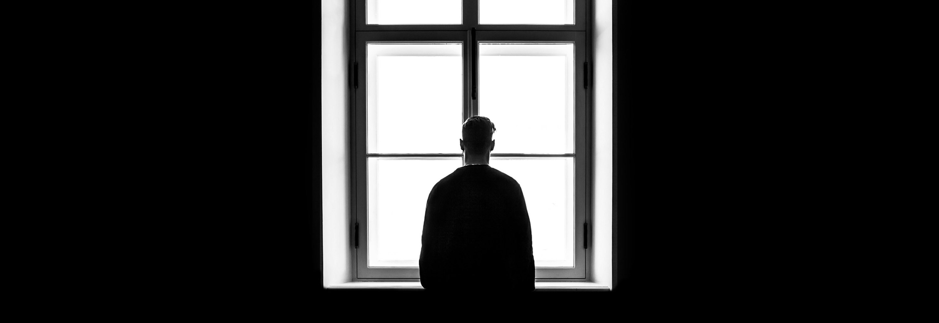 Person standing at window alone. Photo: Sasha Freemind/Unsplash