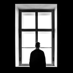 Person standing at window alone. Photo: Sasha Freemind/Unsplash