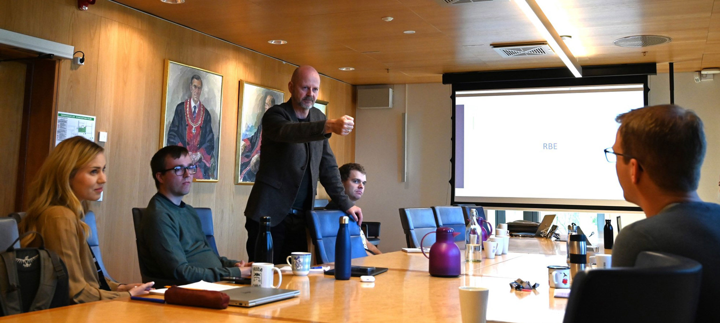 Mann lener seg over møtebord og holder hånden som en mikrofon opp mot en kursdeltager