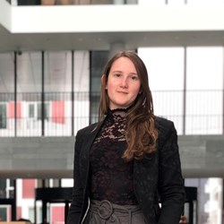 Portrettbilde av en ung dame med mørkt langt hår og blå øyne som ser rett i kamera. 