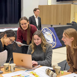 Four students sit around a Mac, smiling and deeply engaged as they collaborate on an assignment during a CEMS seminar at NHH.