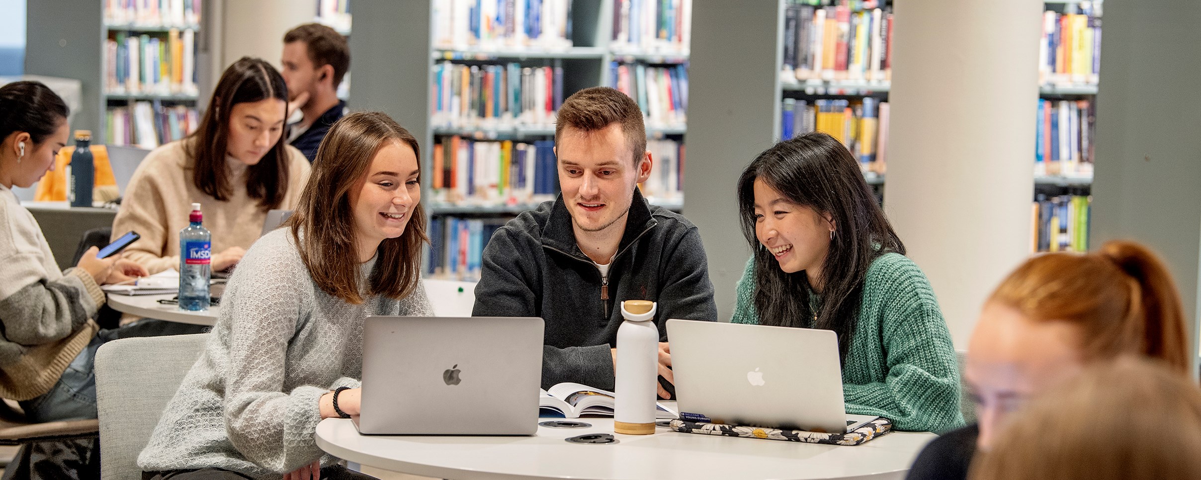 Bilde av tre NHH-studenter som er på biblioteket og ser på PC-skjermer, mens de ler.Foto: Helge Skodvin