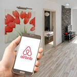 Hand holding a mobile phone with the airbnb logo displayed on it.